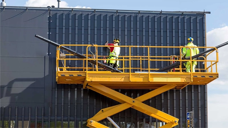 Two construction workers are performing maintenance work on the building's facade on a scissor lift with a double extension platform