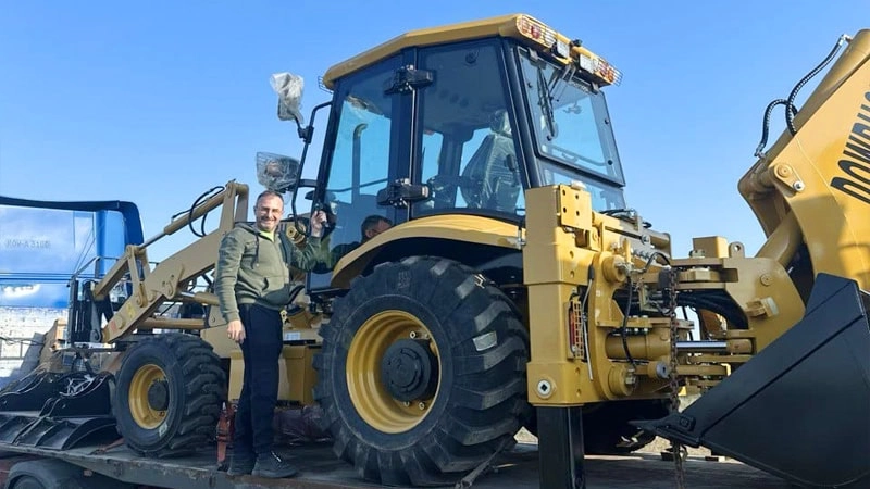 The customer who received the backhoe and accessories took a photo with the machine on the transporter