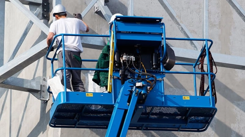 Construction workers wearing protective equipment stand on the working platform of a boom lift and work at height.